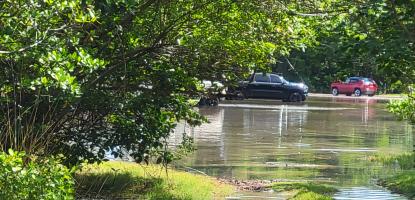 Sunny day a shallow pool of water covers a parking lot with two cars in the background